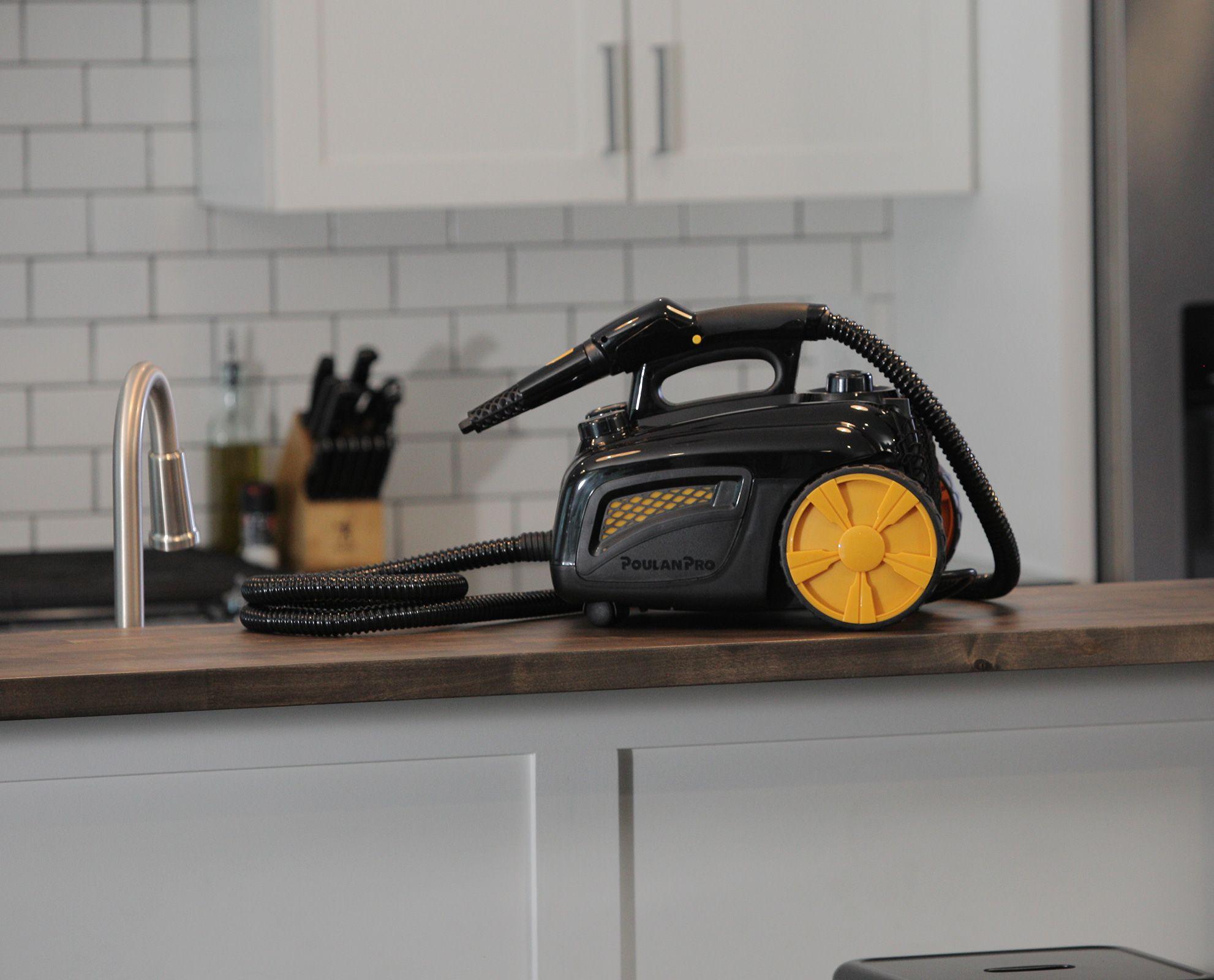 Image of the Poulan Pro PP350 side angle on top of a wooden countertop with white cabinetry underneath. The image contains a wrapped up hose with the jet nozzle attachment on top of the steam cleaner.