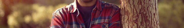Man in Blue and Red Flannel leaning on a tree.