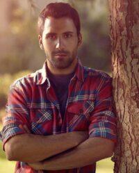 Man in flannel leaning against a tree